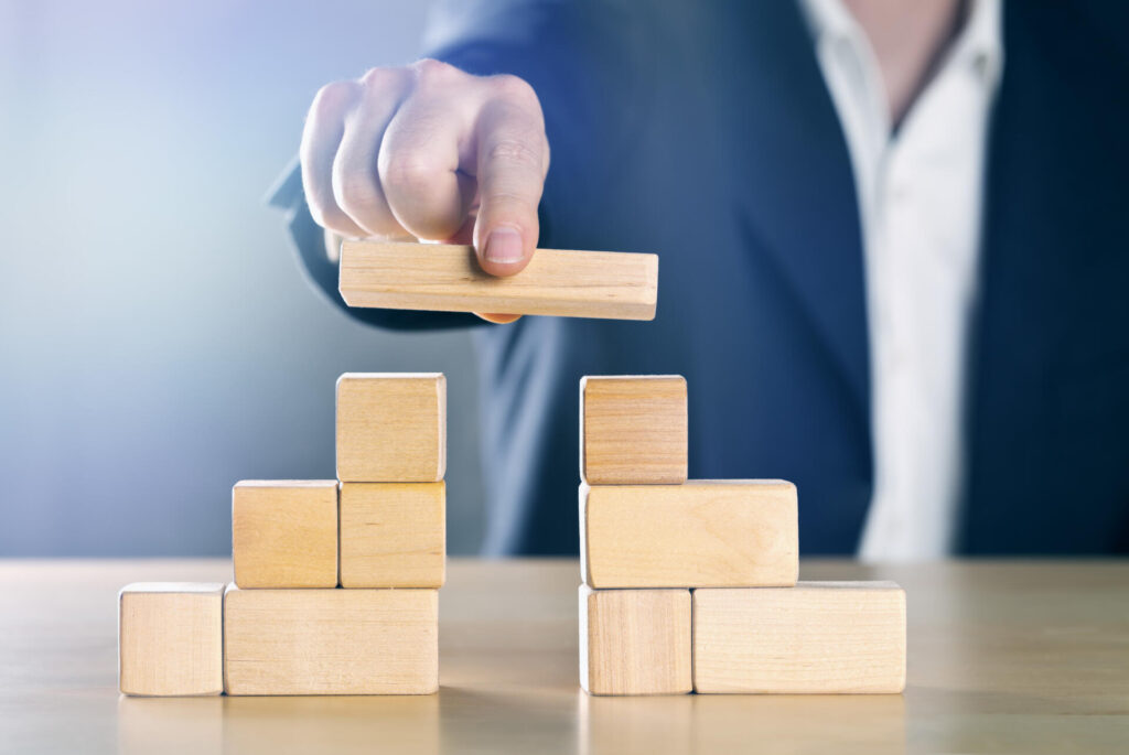 Business man bridging the gap between two towers or parties made from wooden blocks