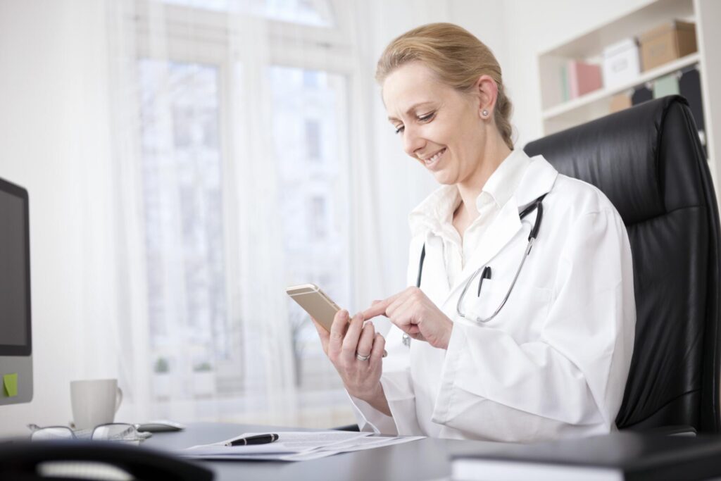 Female Doctor at her Table Browsing on her Phone